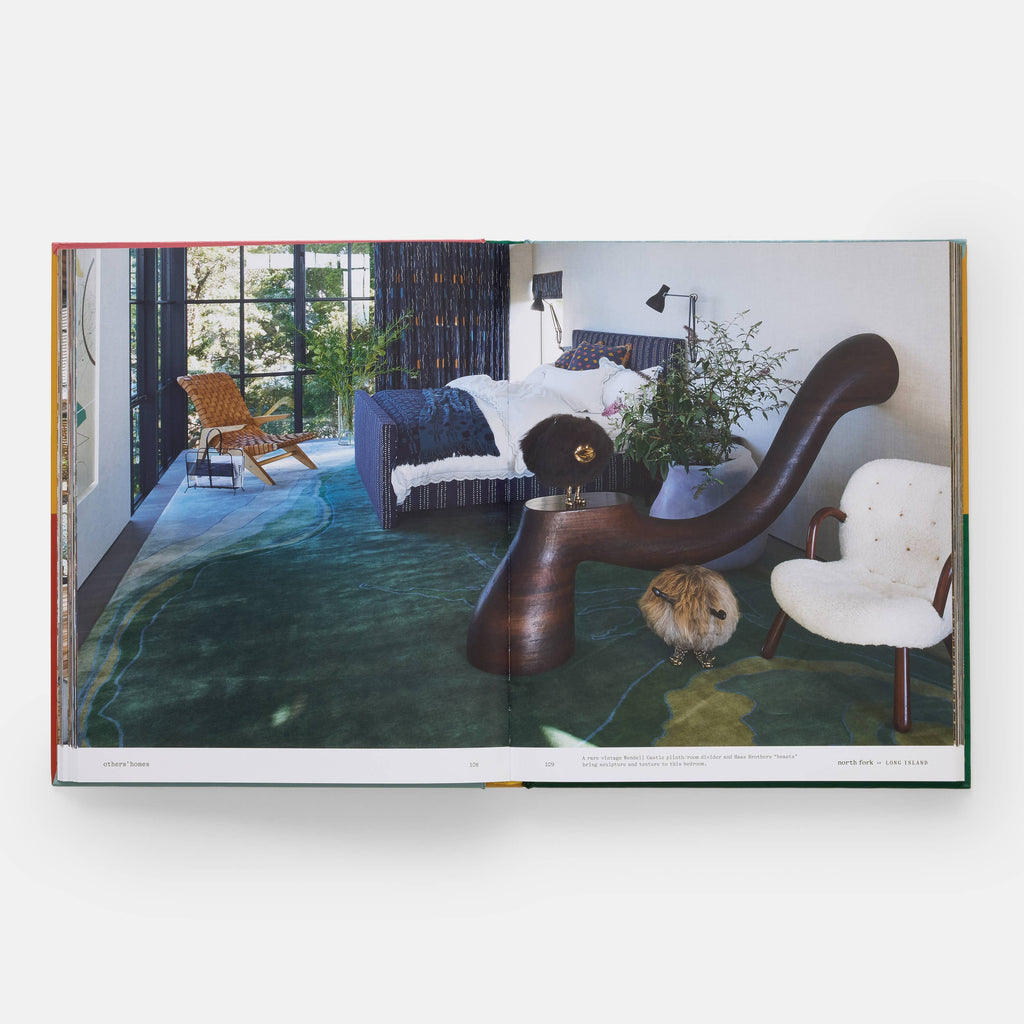 Modern living room with a unique brown chair, white armchair, and a bed in the background.