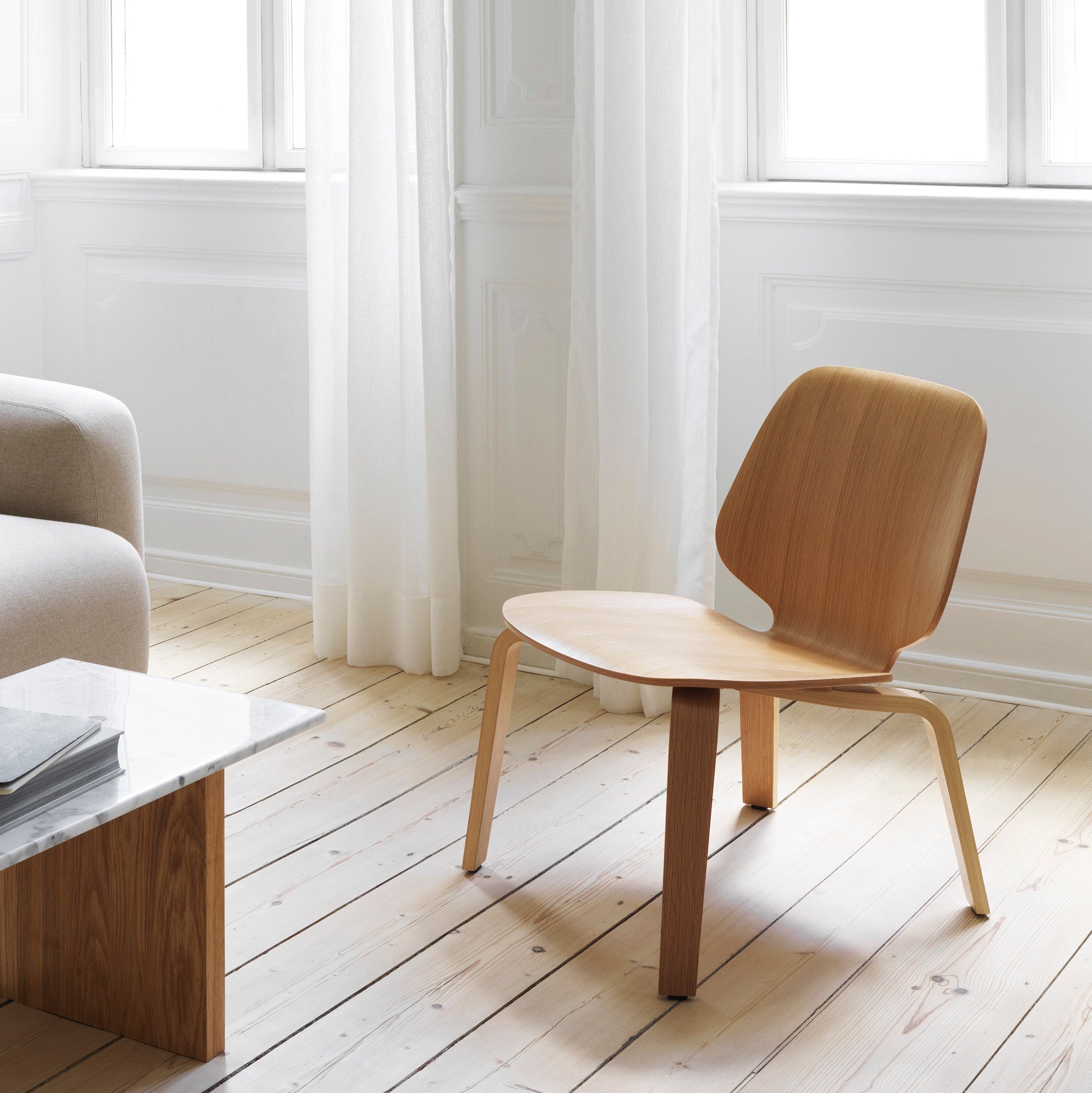 Wooden chair in a minimalistic room with light wood flooring and white walls.
