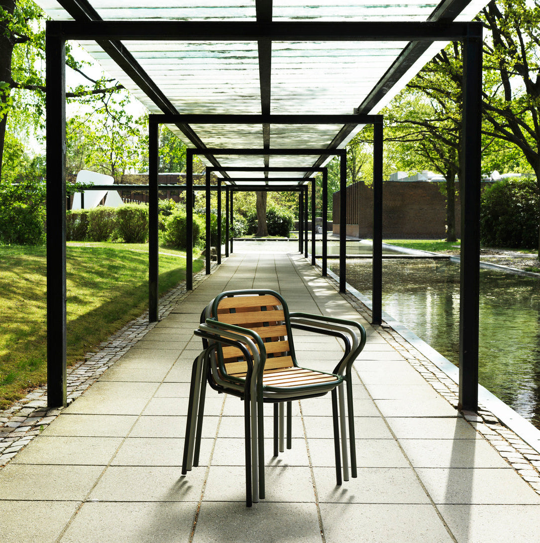 Modern outdoor setting with a covered walkway and chair, surrounded by greenery.