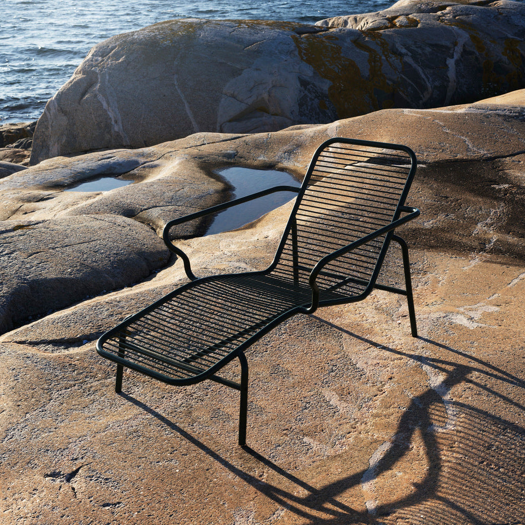 Black metal lounge chair on a rocky coastal landscape with ocean in the background