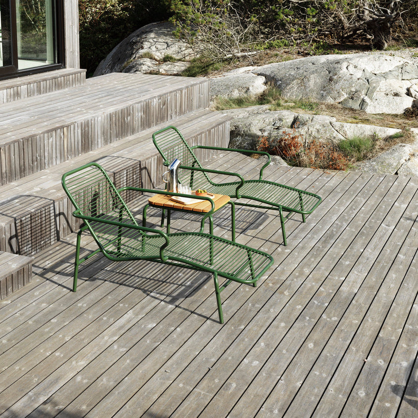 Outdoor seating area with green metal chairs on a wooden deck, surrounded by natural landscape.