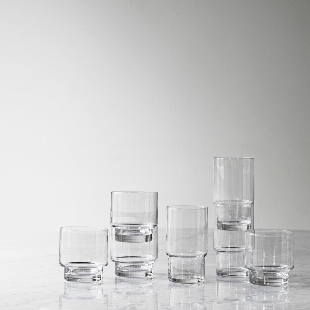 Set of clear glass tumblers on a reflective surface with a light gray background