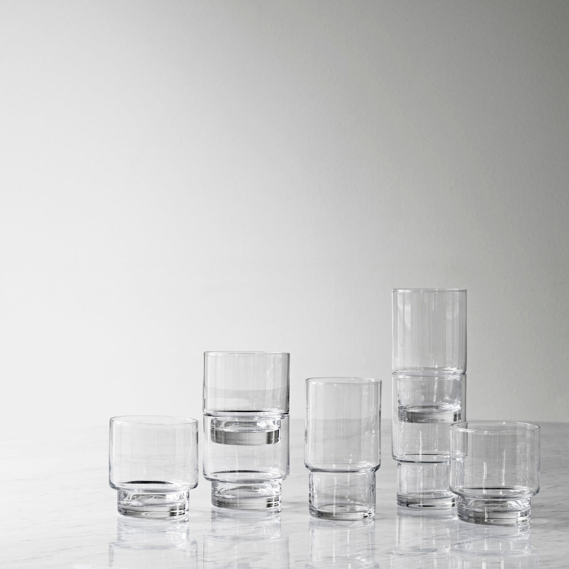 Set of clear glass tumblers on a reflective surface with a light gray background