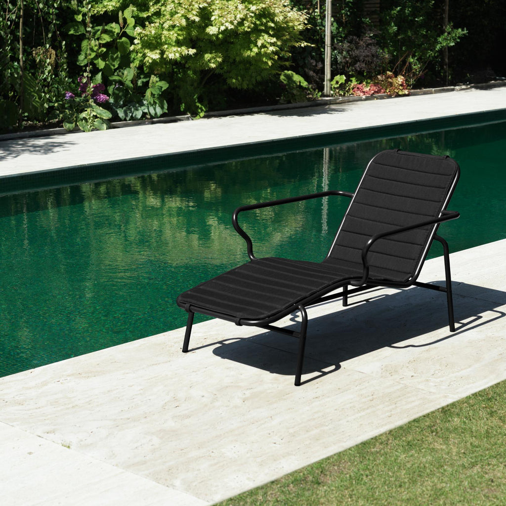 Black lounge chair by a pool with greenery in the background