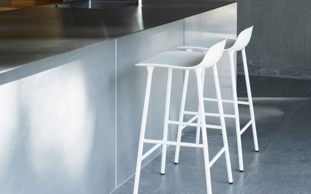 White bar stools in front of a metallic kitchen counter.