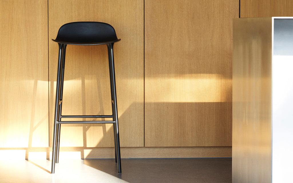Black bar stool against a wooden wall with a light source casting shadows.