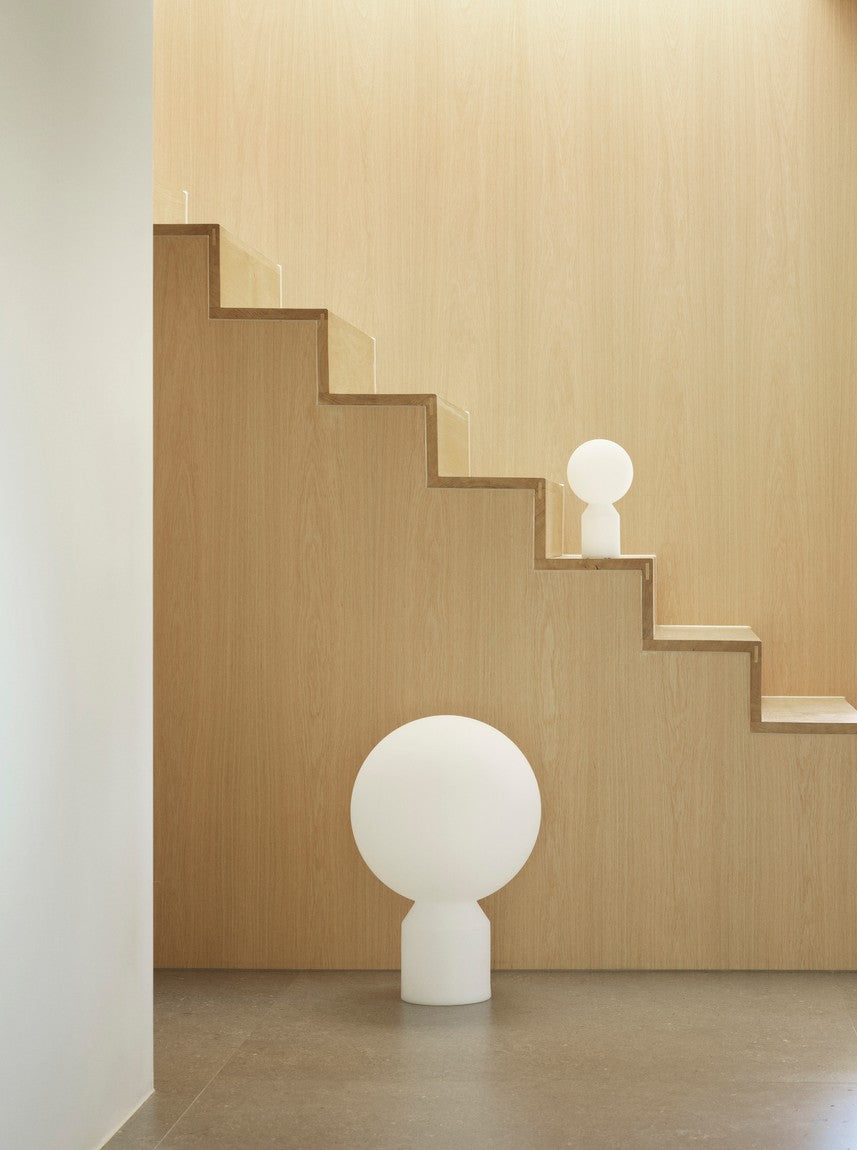 Modern white floor lamp on a wooden staircase with a neutral color scheme.