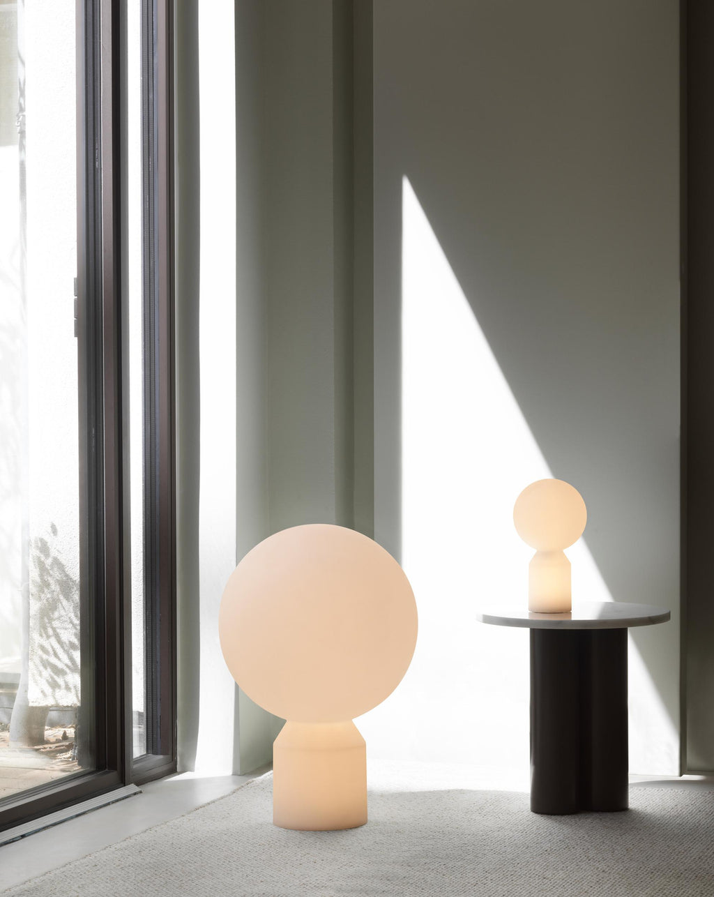 Two spherical lamps on a table next to a large window with curtains.