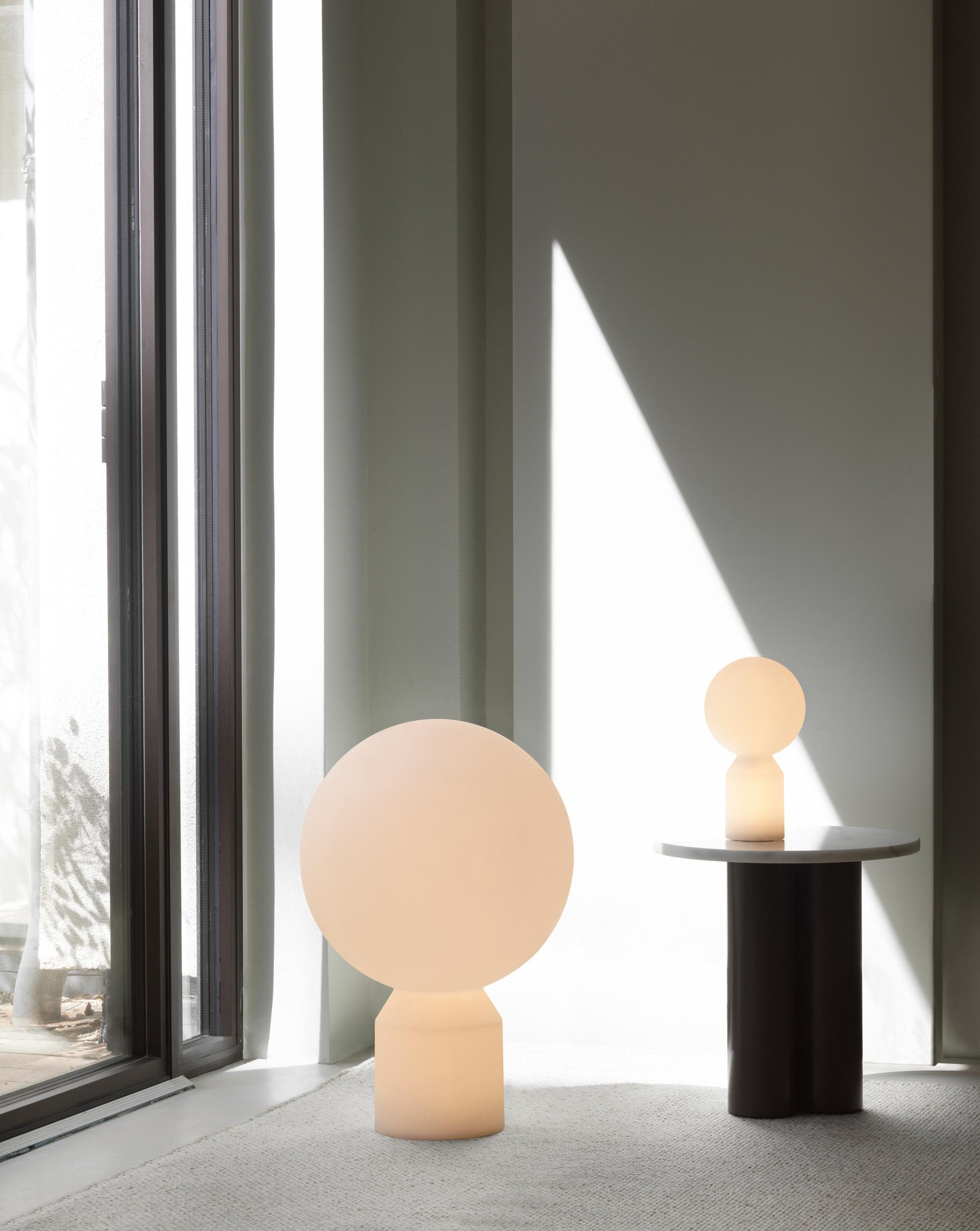 Two spherical lamps on a table next to a large window with curtains.