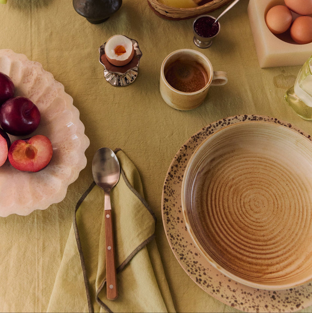 Breakfast table setting with plates, cups, and food items on a yellow tablecloth.