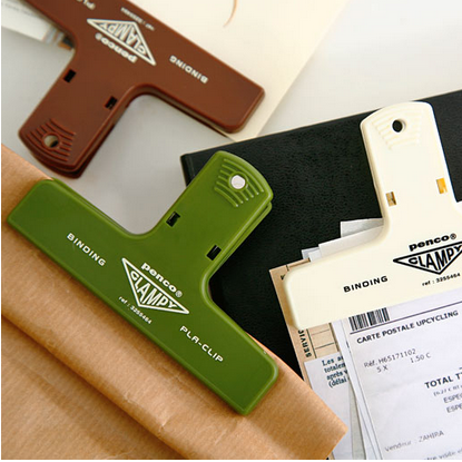 Green Denco Clamp Plus Clip on a white surface with office supplies in the background