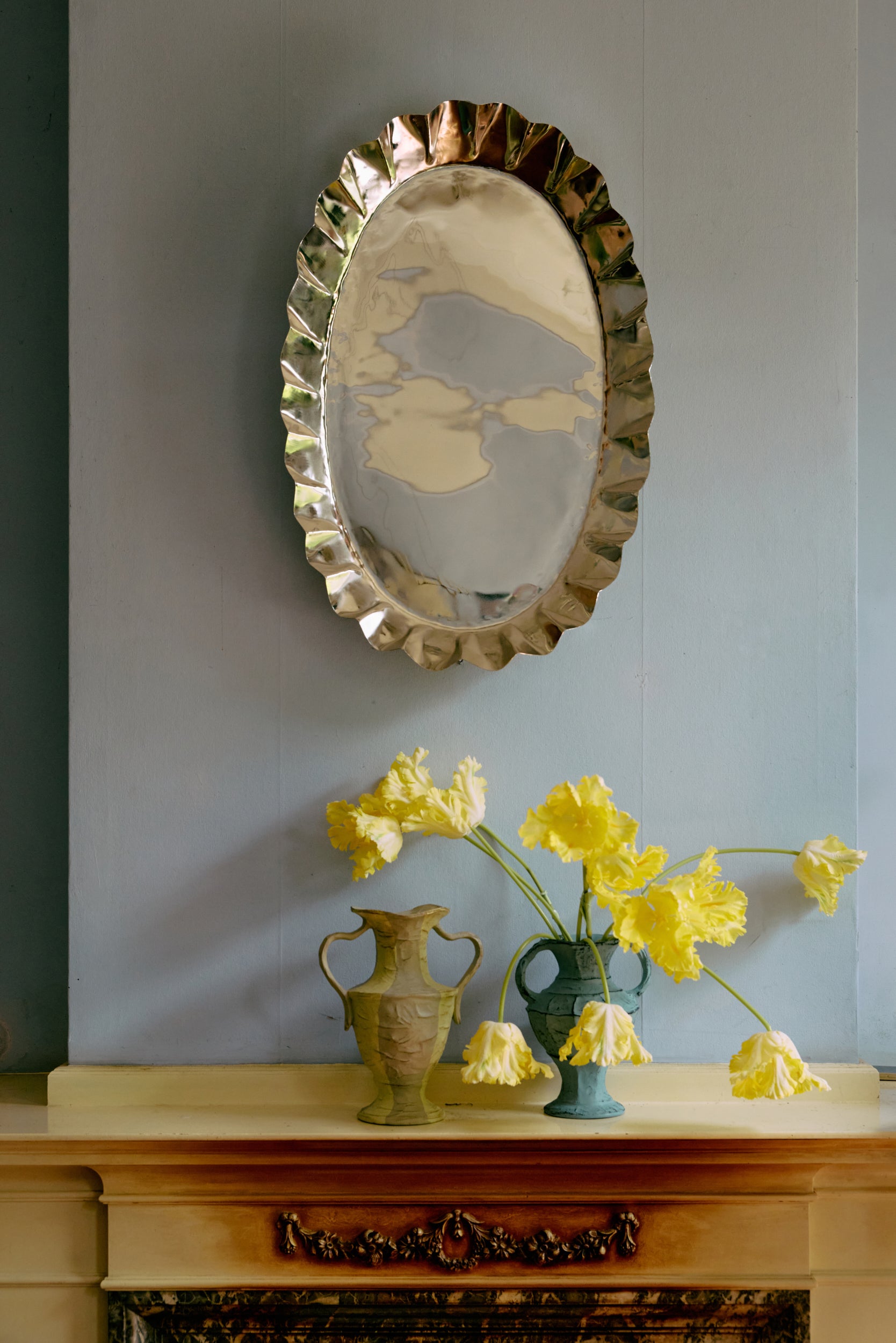 Decorative mirror with floral design above a mantelpiece with vases and flowers.