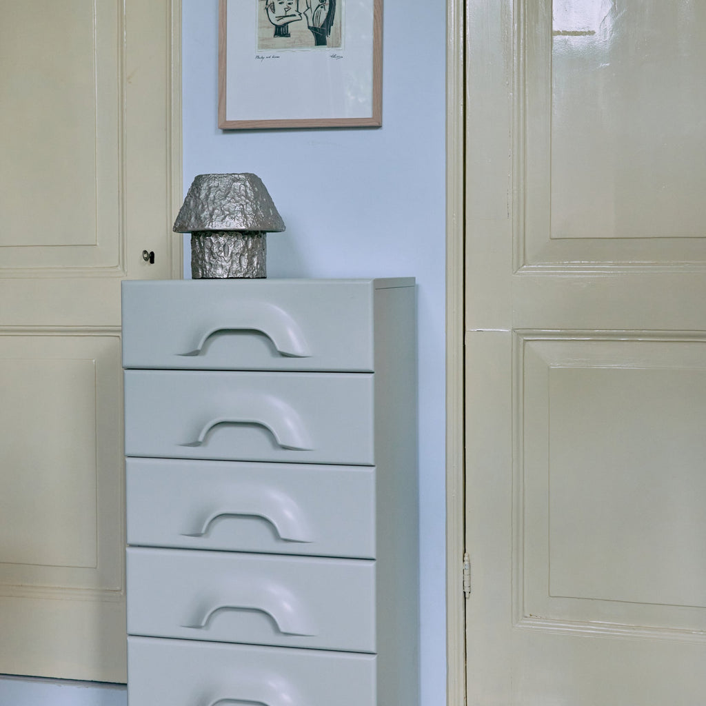 White dresser with five drawers against a light blue wall with a framed picture.