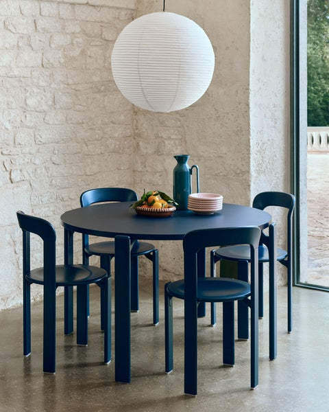 Modern dining set with a round blue table and chairs in a room with a stone wall and large window.