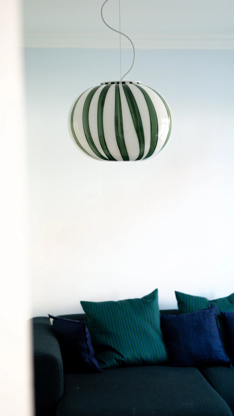 Striped pendant light hanging above a dark green sofa with blue cushions.