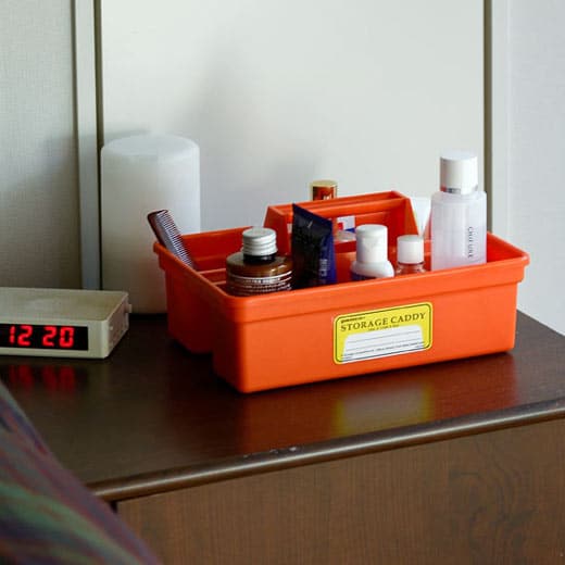 Orange storage caddy with various items on a surface next to a clock.
