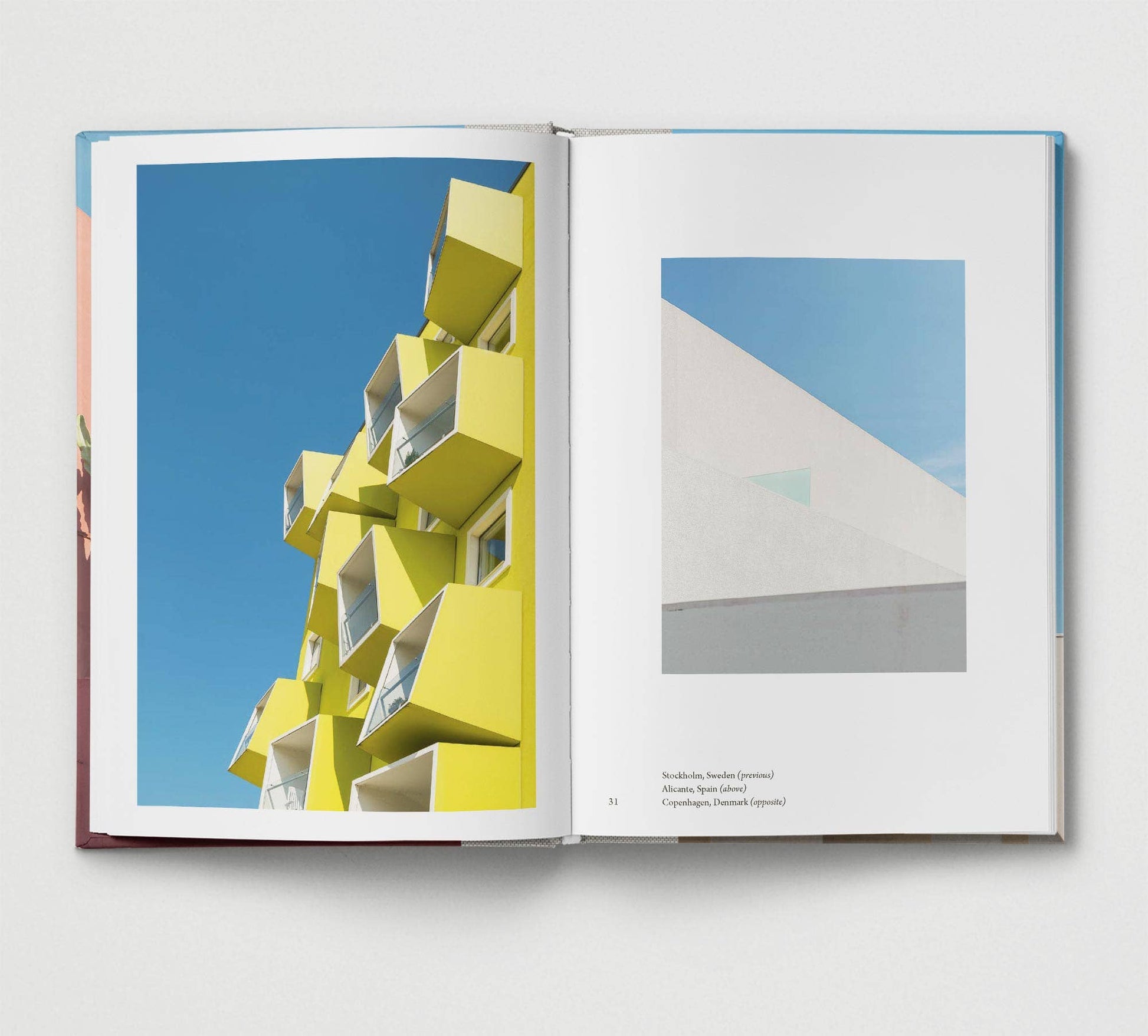 Open book showing images of modern architecture with a yellow building and blue sky on one page, and a white building on the other.