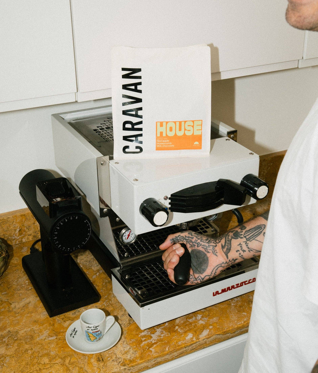 Person using a caravan coffee machine on a wooden counter with a white cup and saucer.