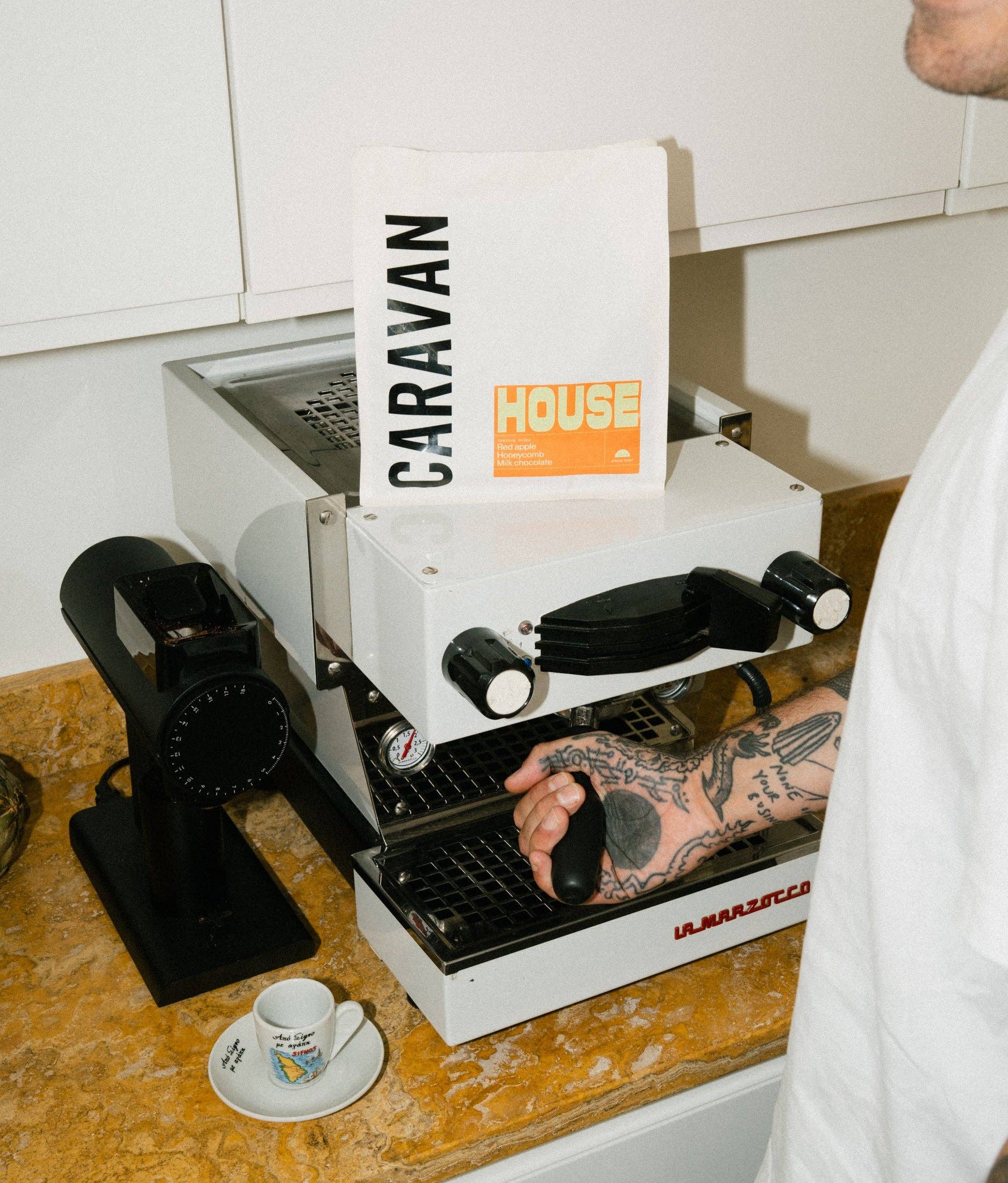 Person using a caravan coffee machine on a wooden counter with a white cup and saucer.