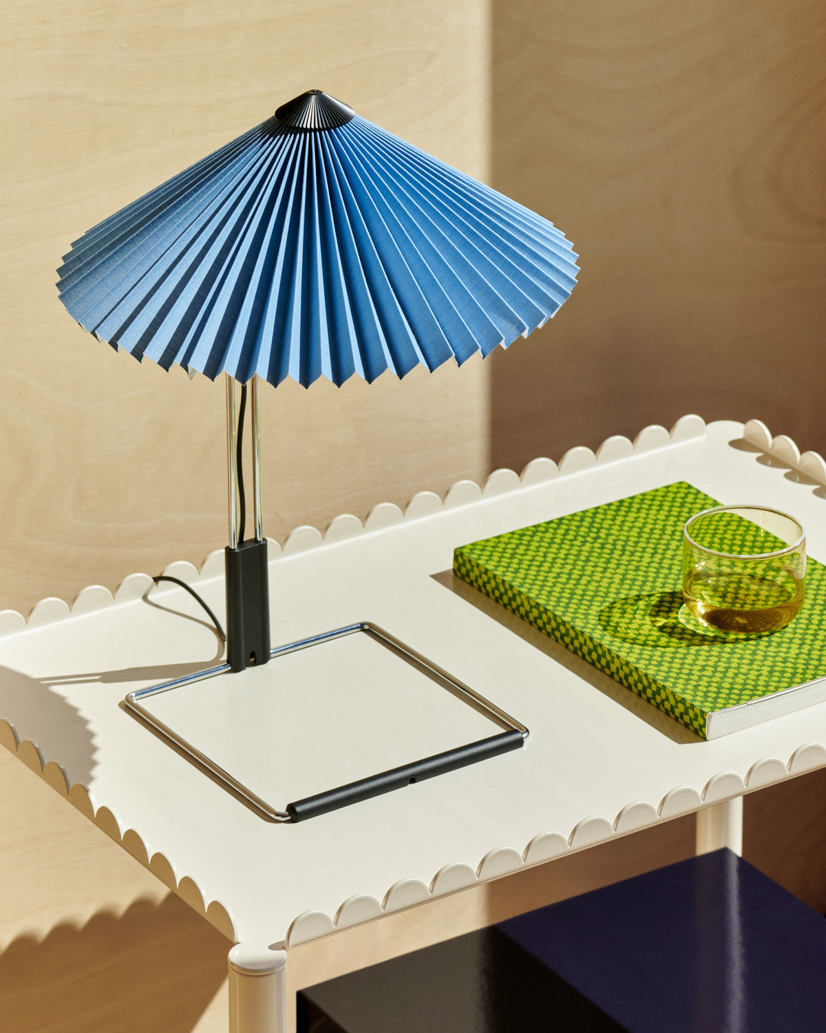 Blue lampshade on a white table with a green cloth and glass.