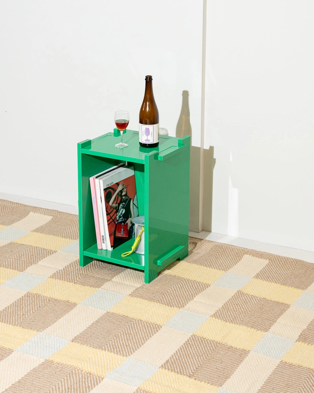 Green side table with books and a bottle on a checkered floor