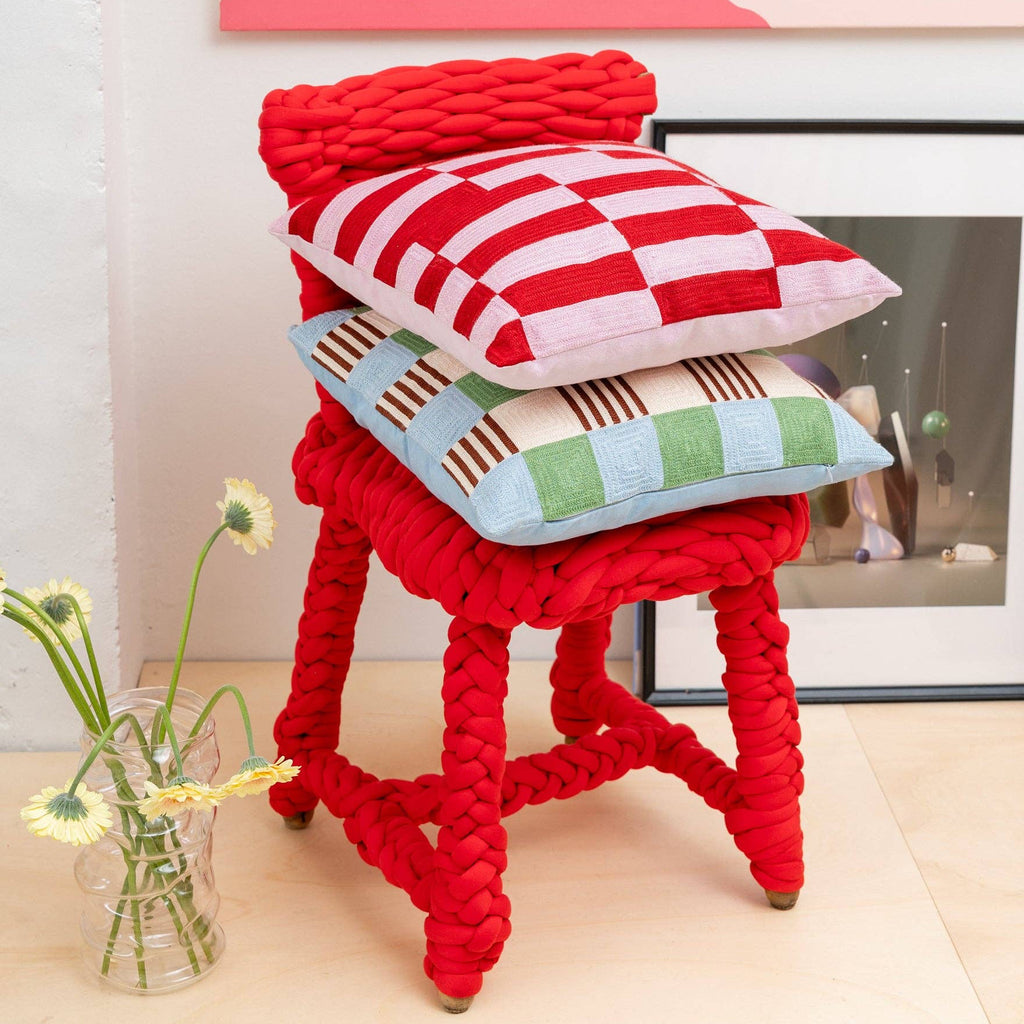 Red woven stool with colorful cushions in a room setting