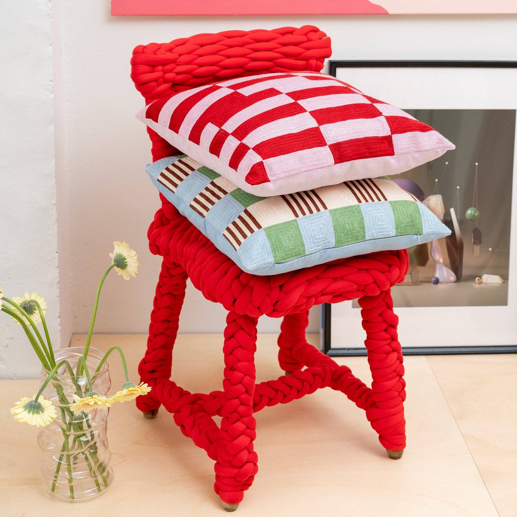 Red woven stool with colorful cushions in a room setting