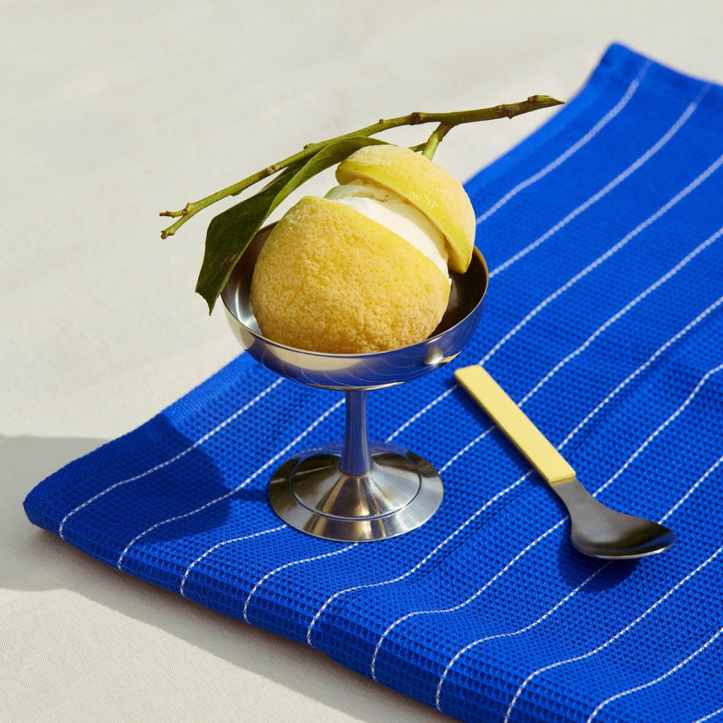 Dessert with a lemon and cream in a silver bowl on a blue striped towel with a spoon.