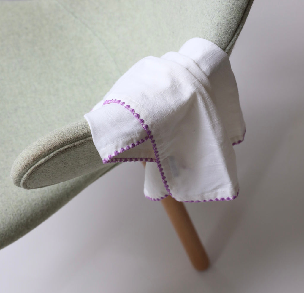 White cloth with purple trim draped over a green chair.