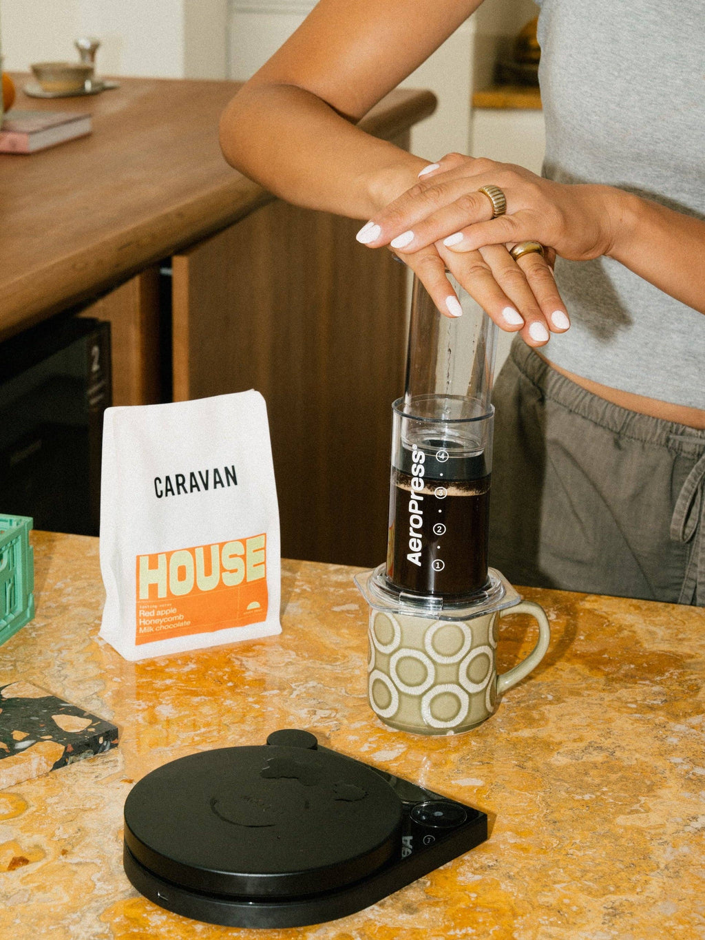 Person making coffee using an AeroPress on a kitchen counter with Caravan Coffee packaging.
