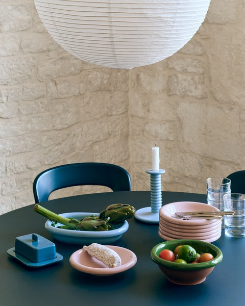 Dining table with ceramic plates, bowls, and a candle holder against a stone wall.