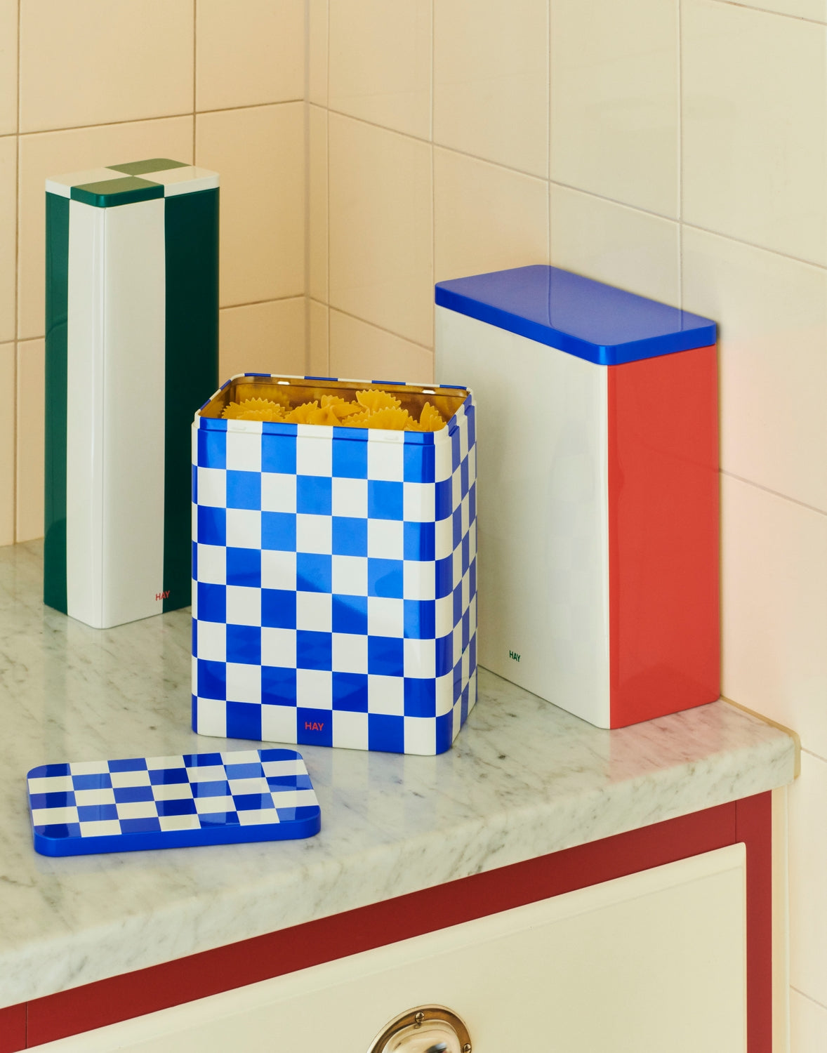 Colorful trash cans and a checkered mat on a tiled bathroom floor.