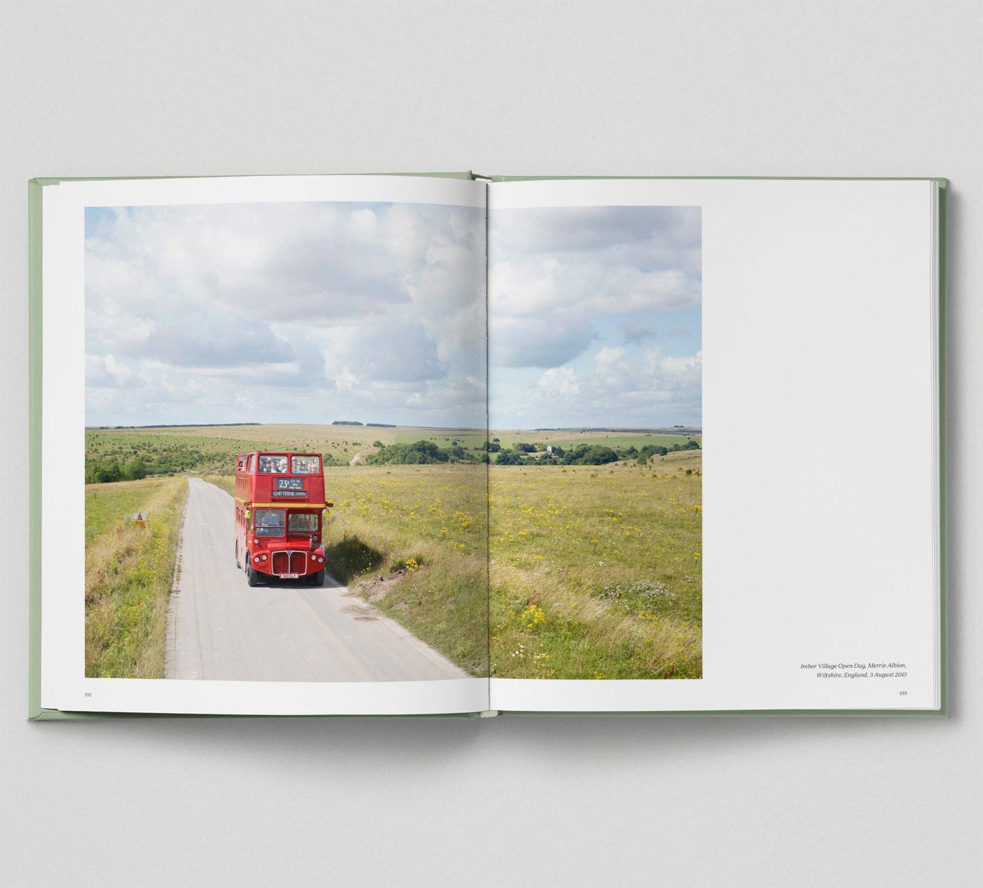 Open book showing a red double-decker bus on a road with green fields and blue sky.