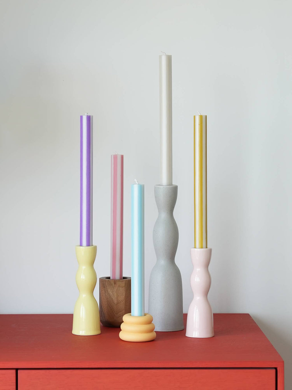 Colorful candles in various holders on a red surface with a white background
