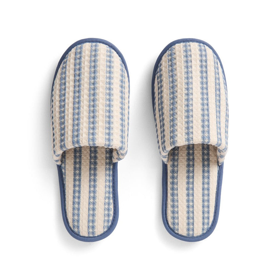A pair of slip-on mule slippers with a cream and blue striped woven pattern and solid blue trim, shown from a top-down view on a white background.
