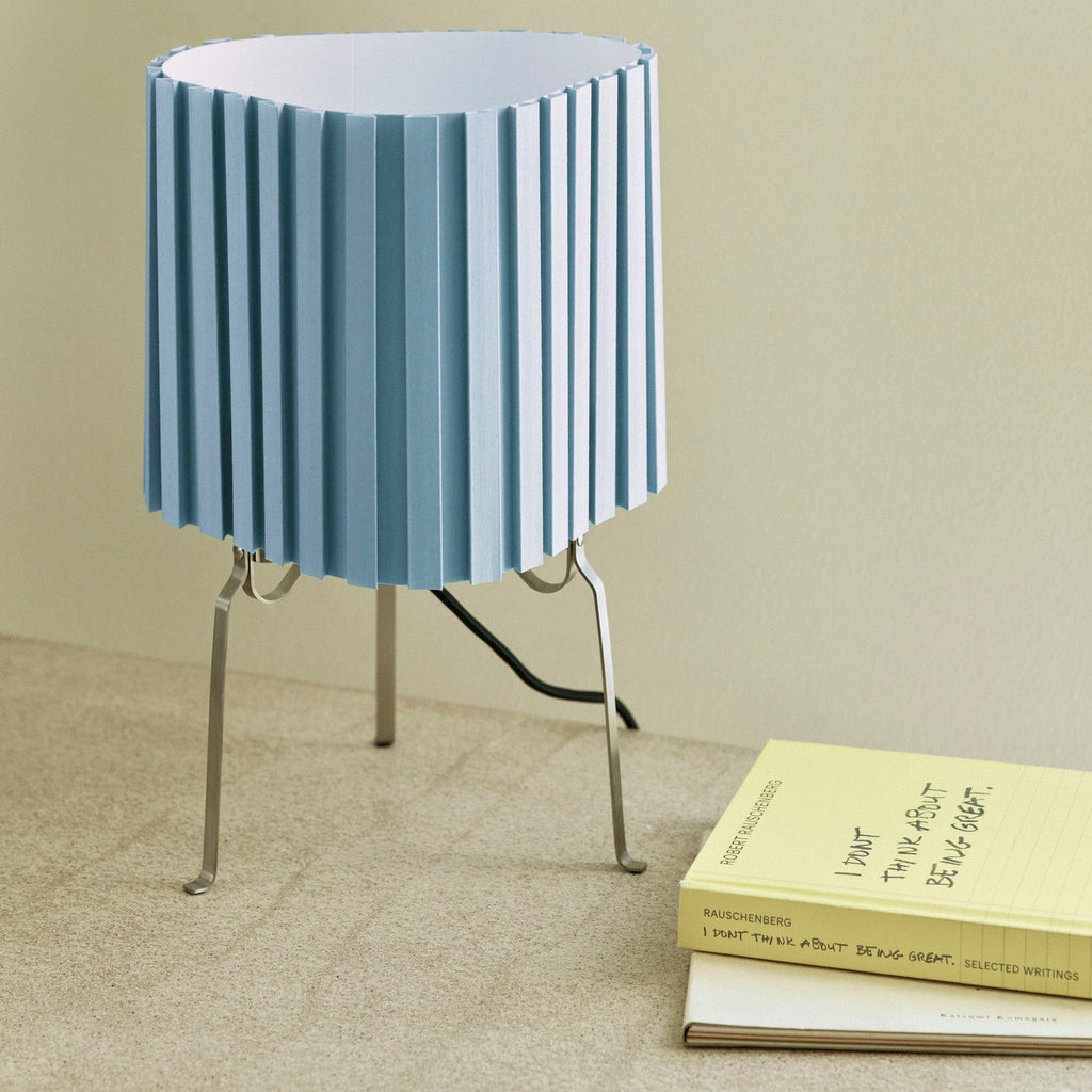 Table lamp with pleated blue shade on a beige surface next to a book
