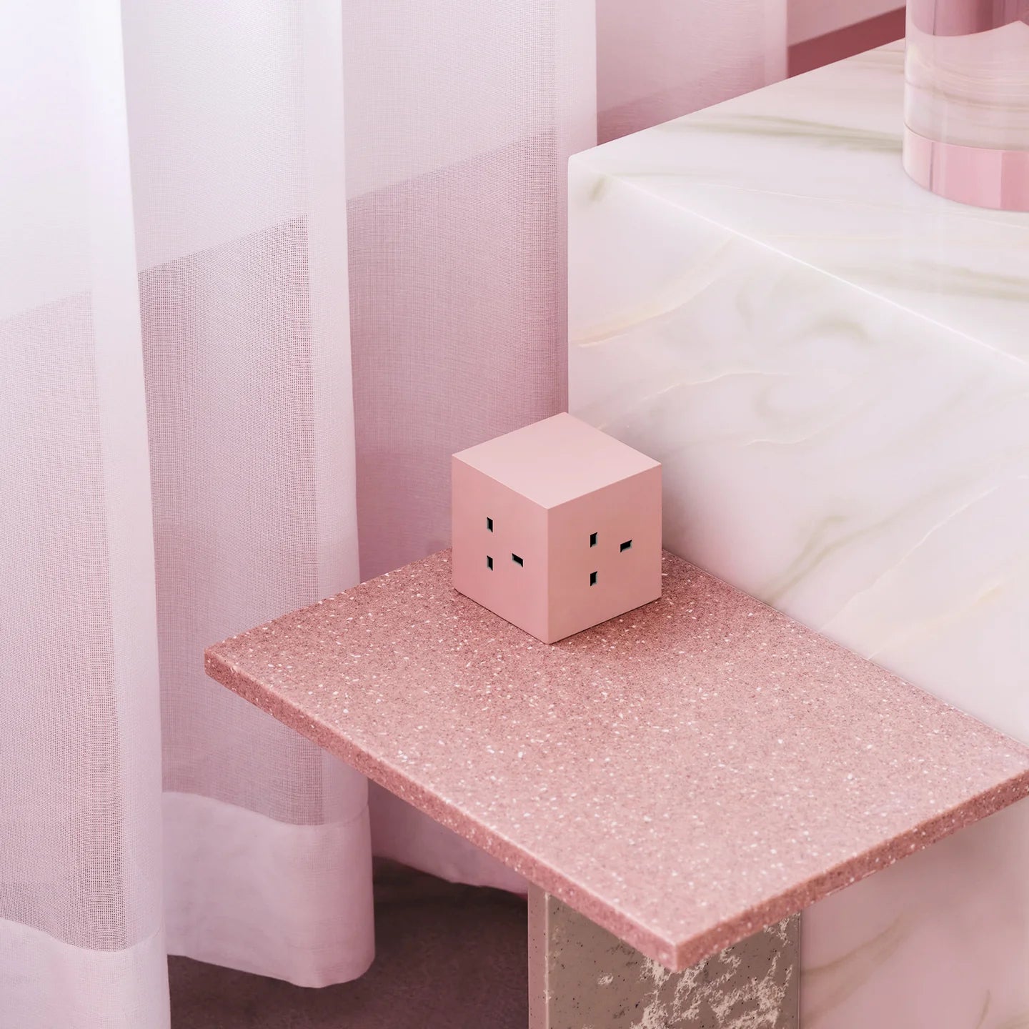 Pink glittery table with a small pink cube on top against a light pink curtain background