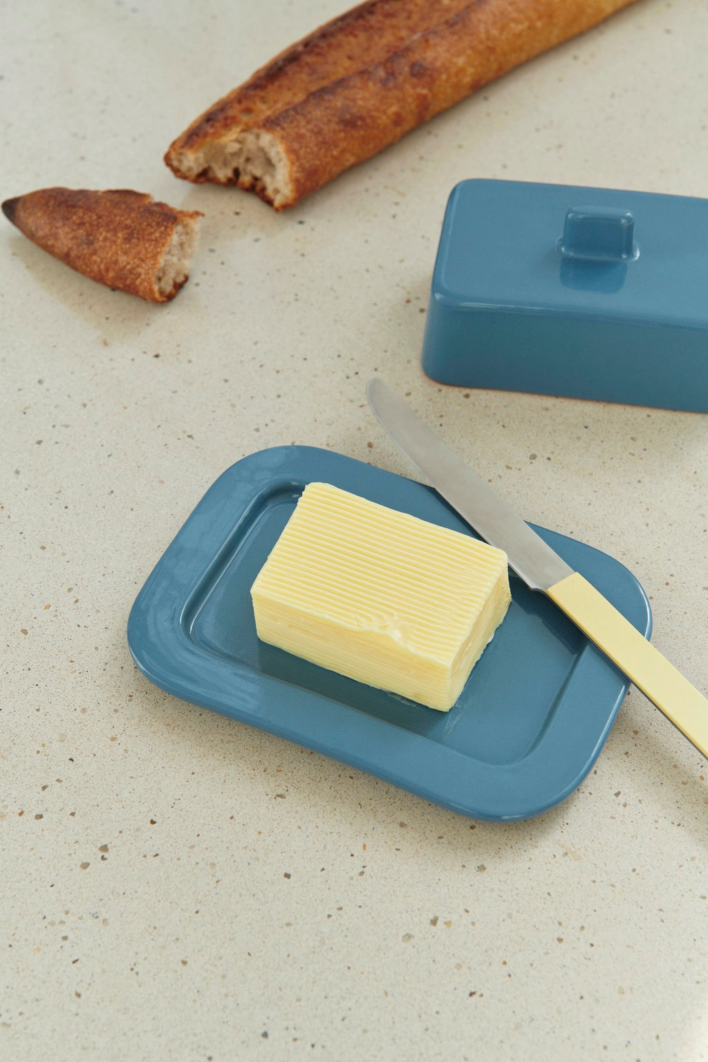 Butter on a blue butter dish with bread and a knife in the background