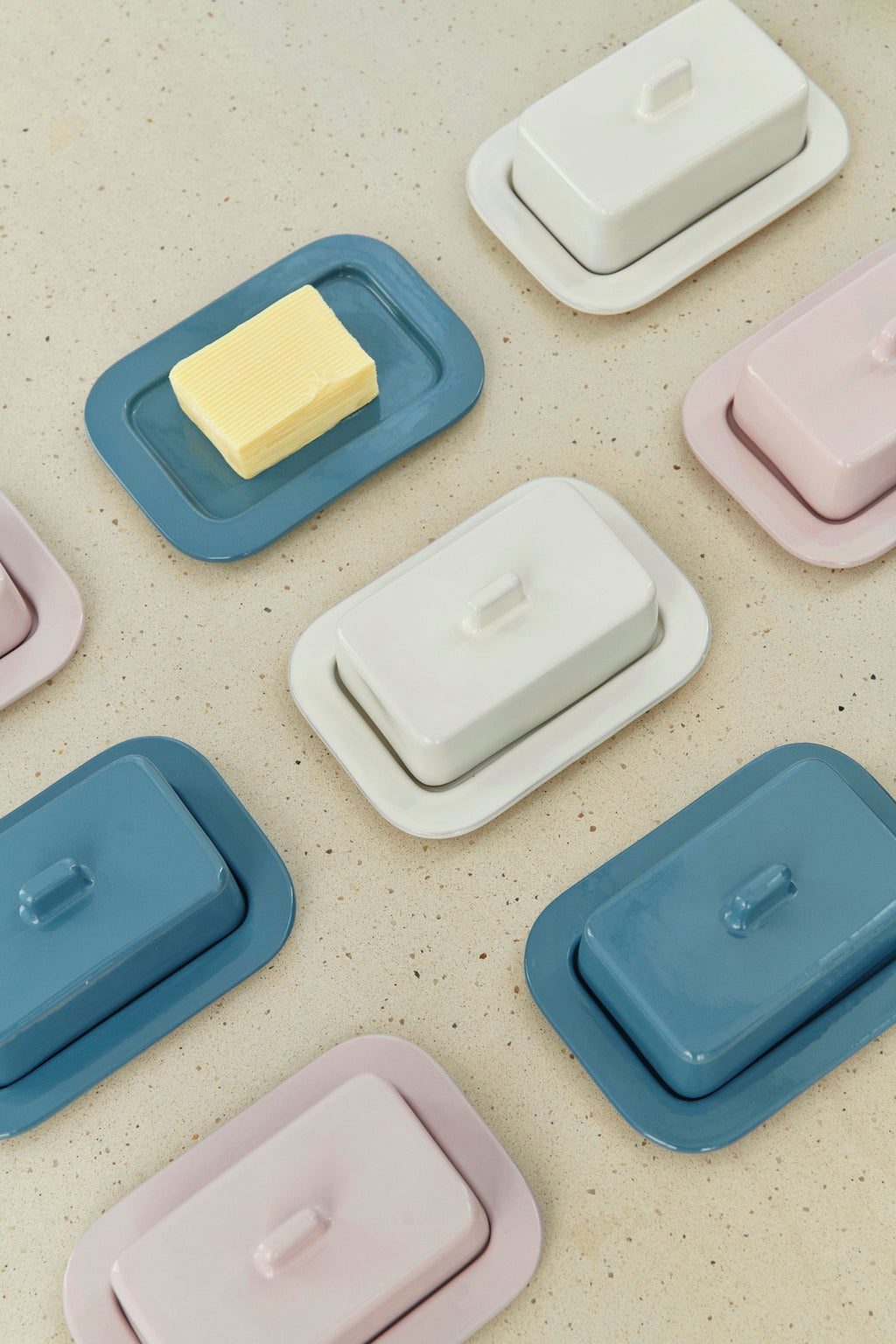 Collection of butter dishes in pastel colors on a speckled surface