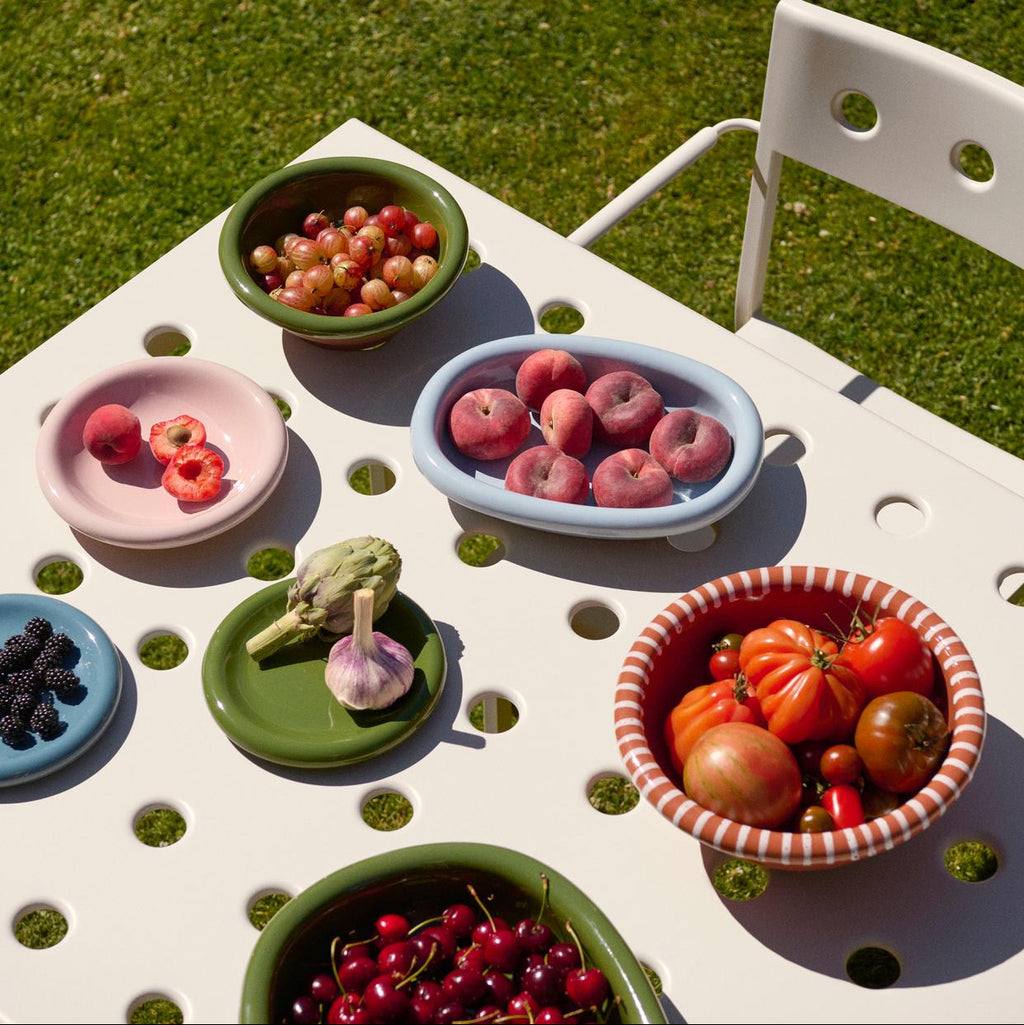 Assorted fruits and vegetables in colorful bowls on a white outdoor table with grass background