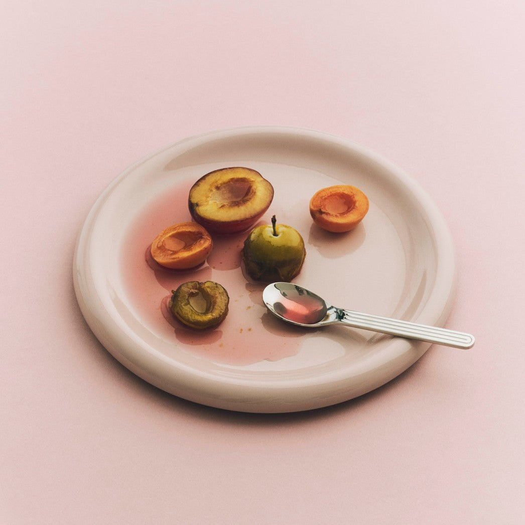 Plated fruit with a spoon on a pink background