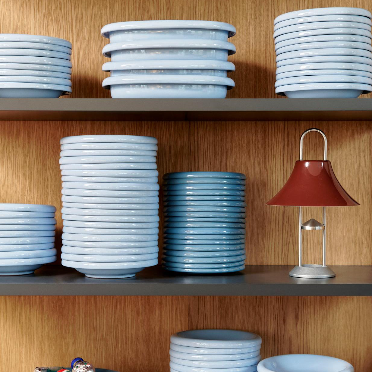 Stacks of ceramic bowls on shelves with a small lamp and figurines.