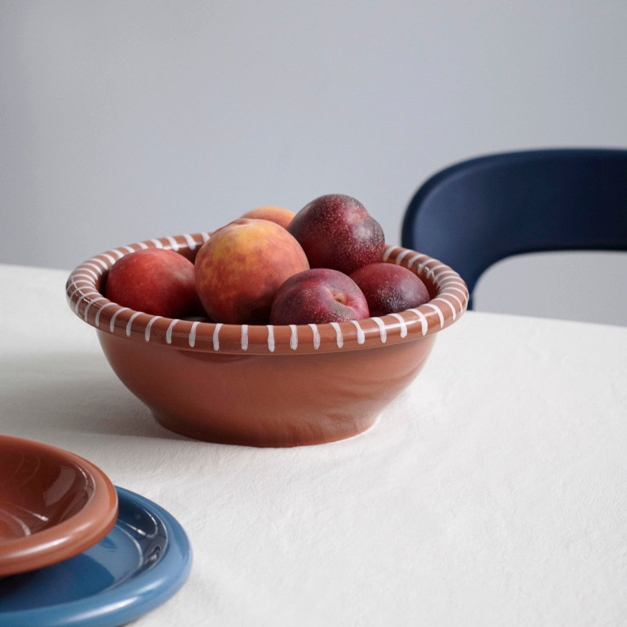 Bowl of plums on a white tablecloth with a blue chair in the background