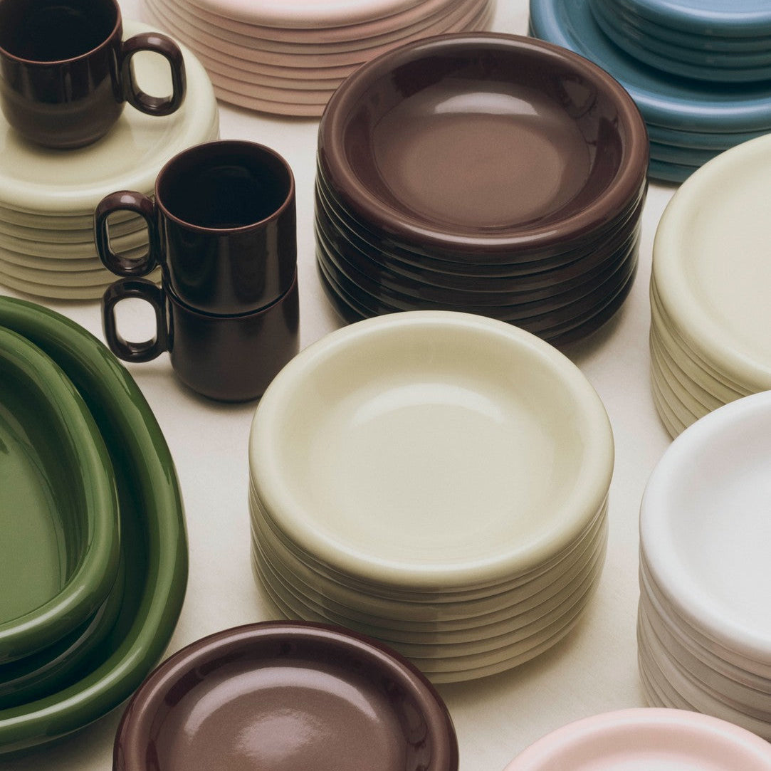 Stacks of colorful ceramic plates and mugs on a white surface