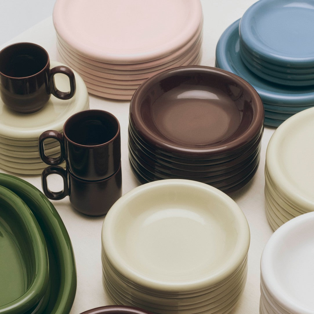 Stacks of colorful ceramic plates and mugs on a white surface