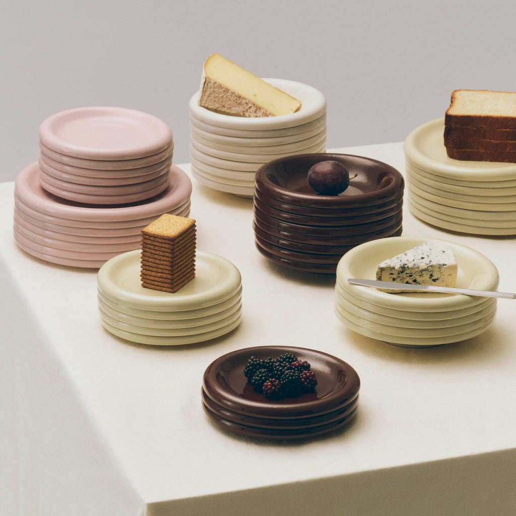 Stacks of ceramic plates in various colors with small desserts on a white surface.