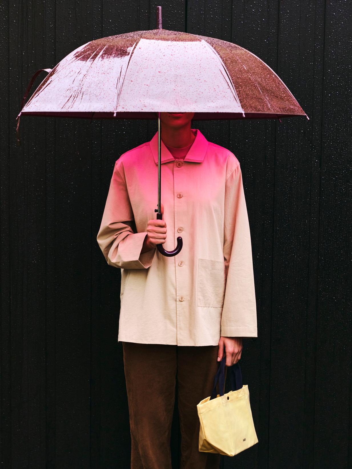 Person holding a clear pink umbrella against a black background