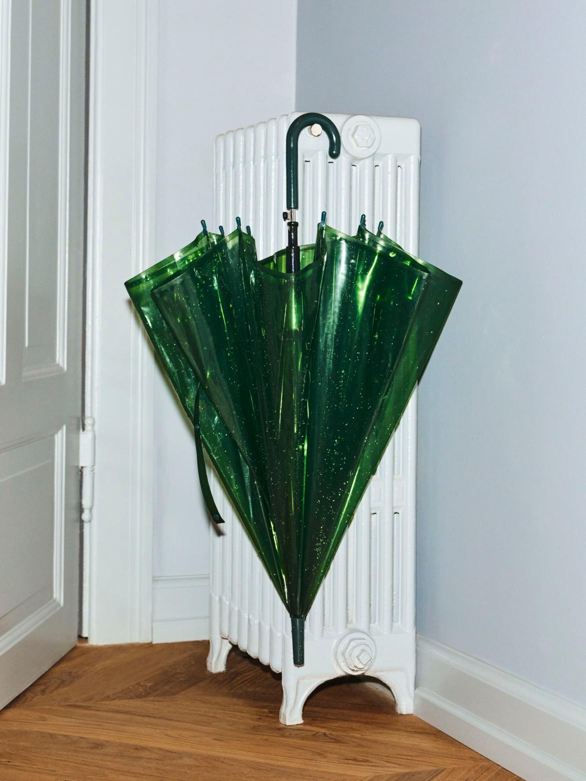 Green umbrella with a unique design standing on a white radiator against a light blue wall.