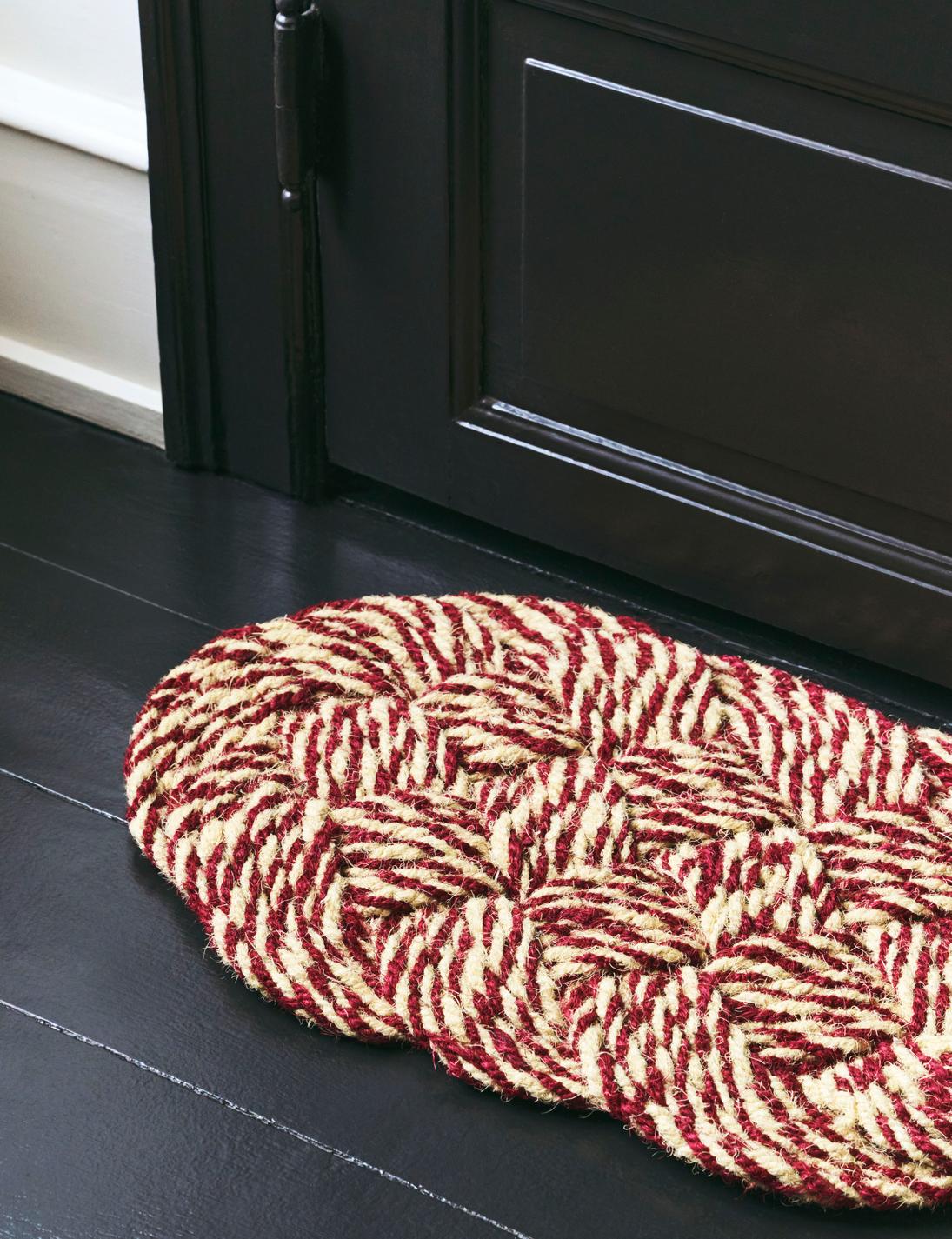 Red and beige braided doormat on a black floor in front of a black door.