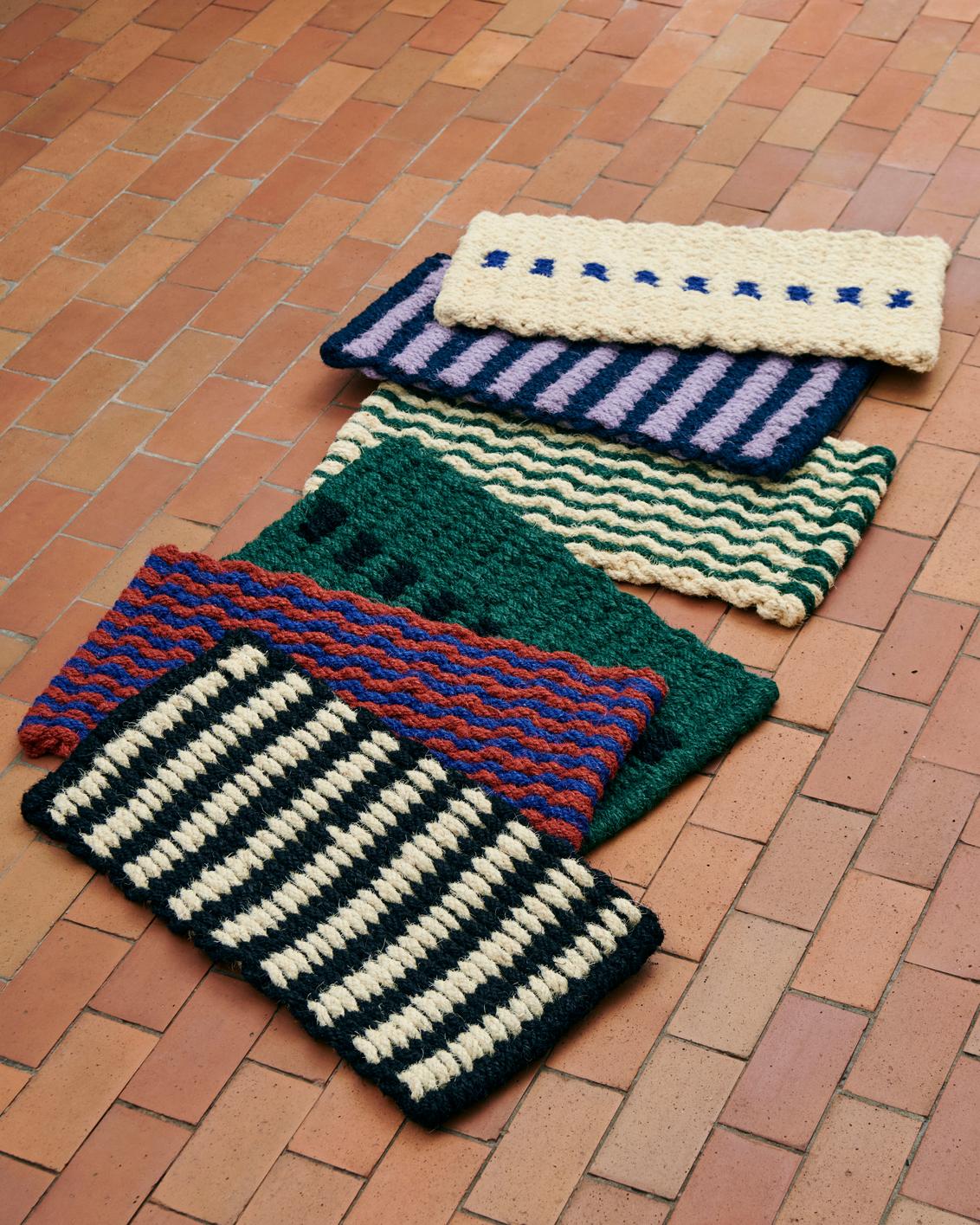 Set of colorful knitted doormats on a brick floor
